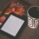 black E-book reader beside white and black mug